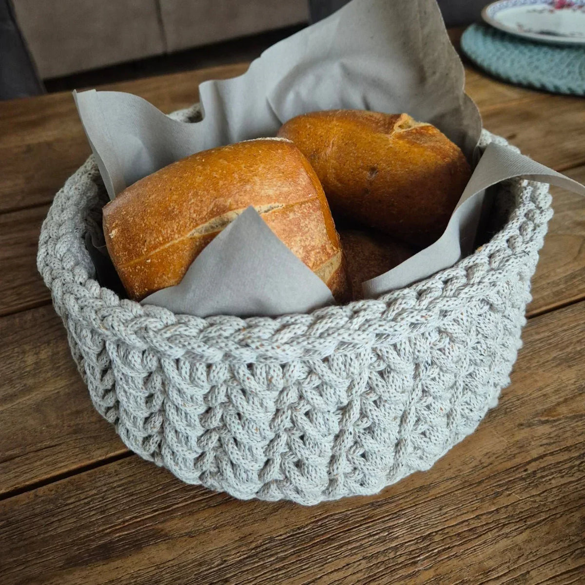 Hellgrauer Brotkorb aus recycelter Baumwolle mit Reliefmuster und Brötchen auf dem FrĂŒhstĂŒckstisch neben Geschirr