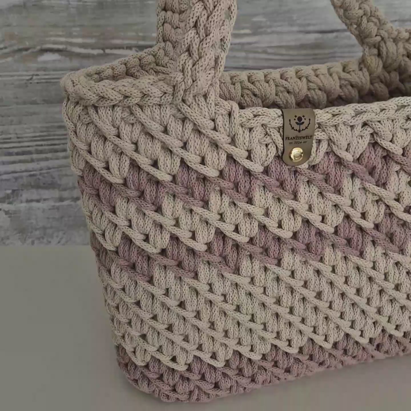 Detailansicht einer handgemachten Häkel-Handtasche in Altrosa und Beige mit Label – aus dicker Baumwollkordel gehäkelt, vor Holzoptik-Hintergrund